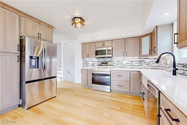 kitchen with light countertops, light wood-style flooring, decorative backsplash, appliances with stainless steel finishes, and a sink