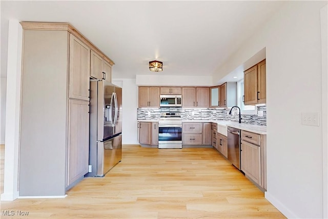 kitchen with a sink, light countertops, appliances with stainless steel finishes, decorative backsplash, and light wood finished floors