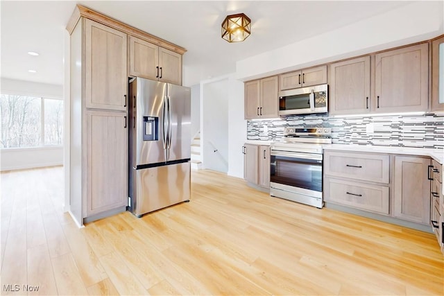 kitchen featuring light wood-style flooring, appliances with stainless steel finishes, light countertops, light brown cabinetry, and backsplash