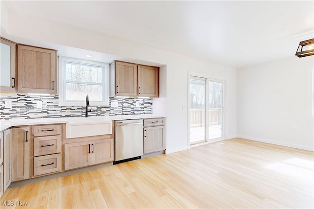 kitchen featuring a sink, light countertops, light wood-type flooring, decorative backsplash, and dishwasher