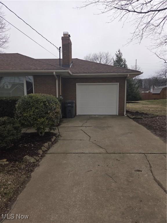 view of front of property with driveway, an attached garage, a chimney, and brick siding