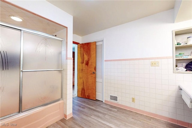 full bath with visible vents, a wainscoted wall, wood finished floors, combined bath / shower with glass door, and tile walls