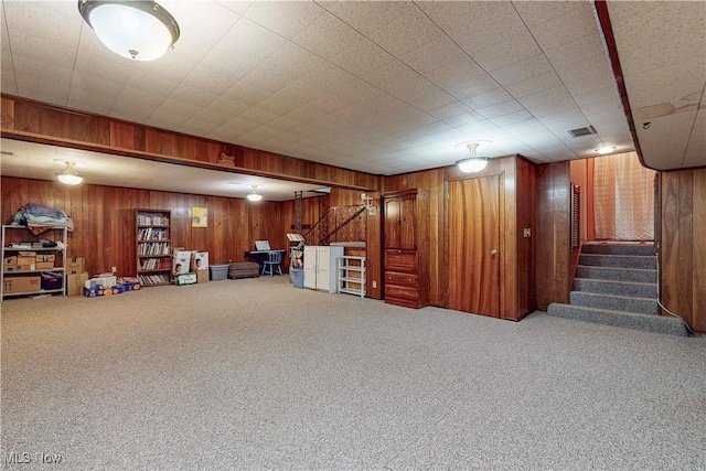 finished basement with wood walls, stairway, carpet flooring, and visible vents