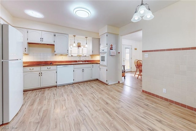 kitchen featuring pendant lighting, tile walls, a sink, light wood-type flooring, and white appliances