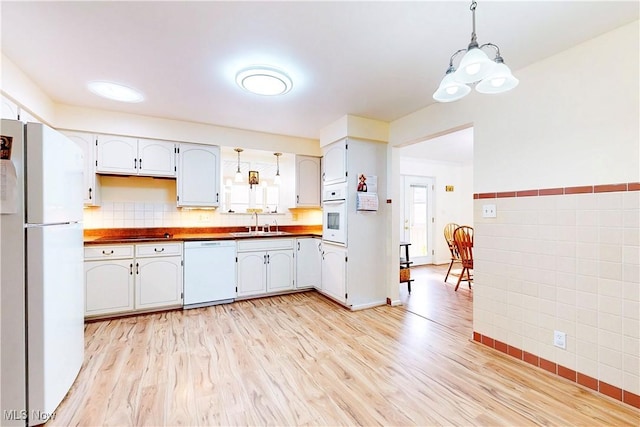 kitchen featuring light wood-style flooring, white appliances, a sink, tile walls, and pendant lighting