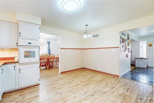 kitchen with a notable chandelier, white cabinetry, visible vents, white oven, and light wood-type flooring