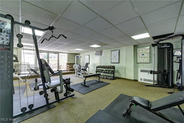 gym with baseboards, a drop ceiling, a wall unit AC, and radiator heating unit