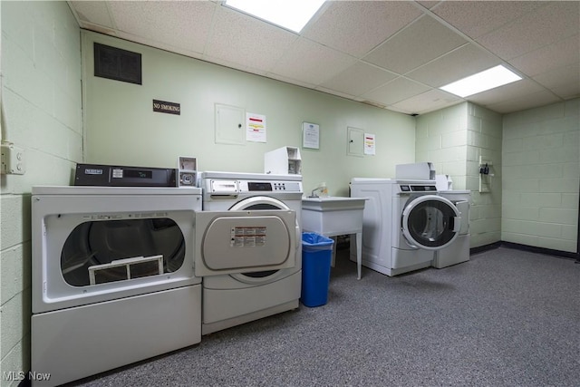 common laundry area with concrete block wall, washer and clothes dryer, and a sink