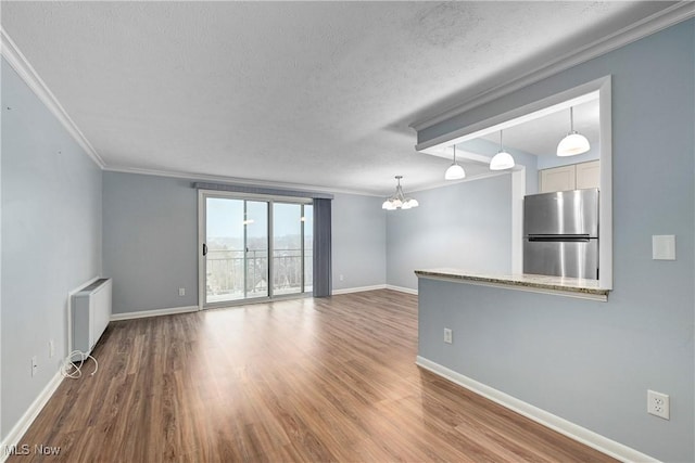 unfurnished living room featuring baseboards, radiator, wood finished floors, crown molding, and a textured ceiling