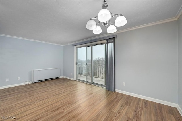 empty room with a notable chandelier, wood finished floors, baseboards, radiator, and crown molding