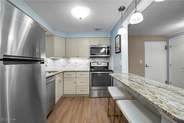 kitchen featuring stainless steel appliances, light wood-type flooring, backsplash, and light stone countertops