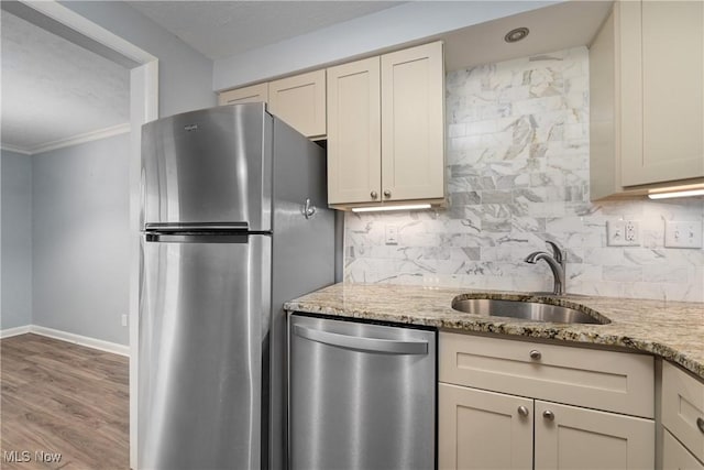 kitchen with decorative backsplash, appliances with stainless steel finishes, a sink, light stone countertops, and baseboards