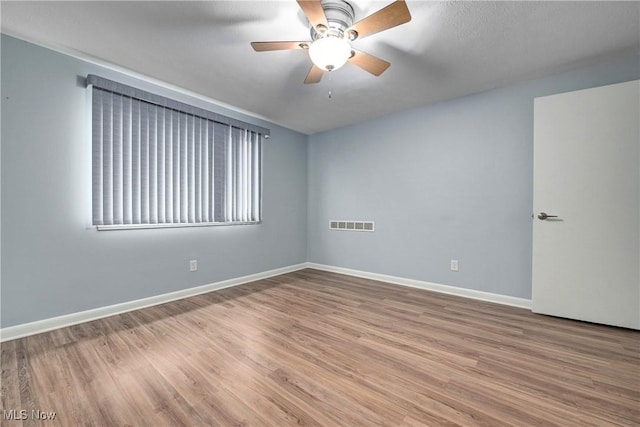 empty room featuring visible vents, ceiling fan, baseboards, and wood finished floors