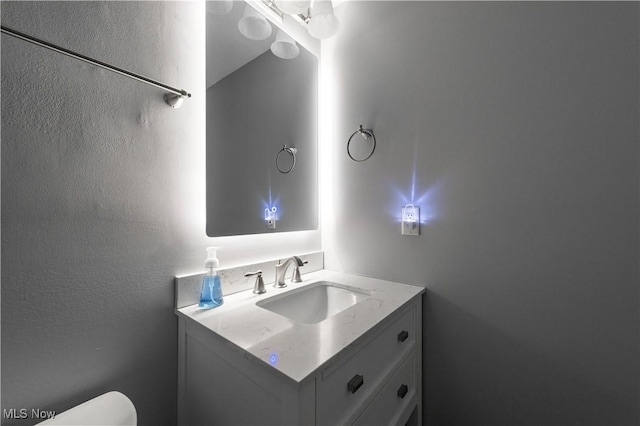 half bath featuring a textured wall, vanity, and toilet