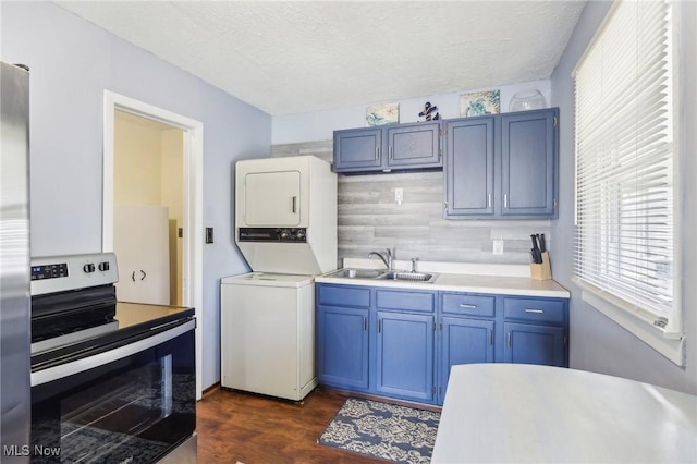 kitchen with electric stove, blue cabinetry, light countertops, stacked washer / dryer, and a sink