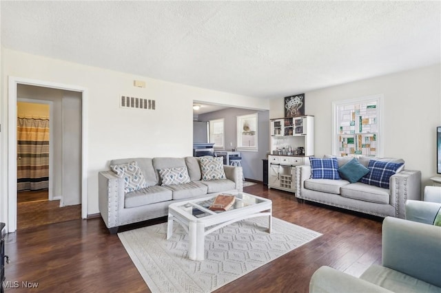 living area with baseboards, a textured ceiling, visible vents, and dark wood-style flooring