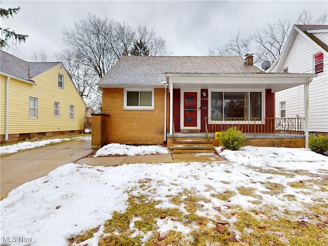 bungalow-style home with covered porch, roof with shingles, brick siding, and a chimney