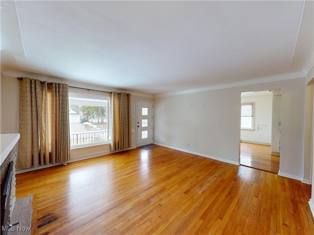 unfurnished living room featuring light wood finished floors, a wealth of natural light, and baseboards