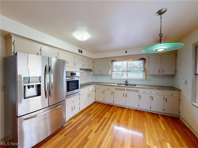 kitchen with light wood finished floors, light countertops, backsplash, appliances with stainless steel finishes, and a sink