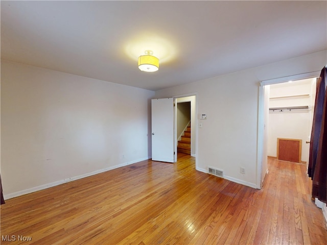 unfurnished bedroom featuring baseboards, a spacious closet, visible vents, and light wood-style floors