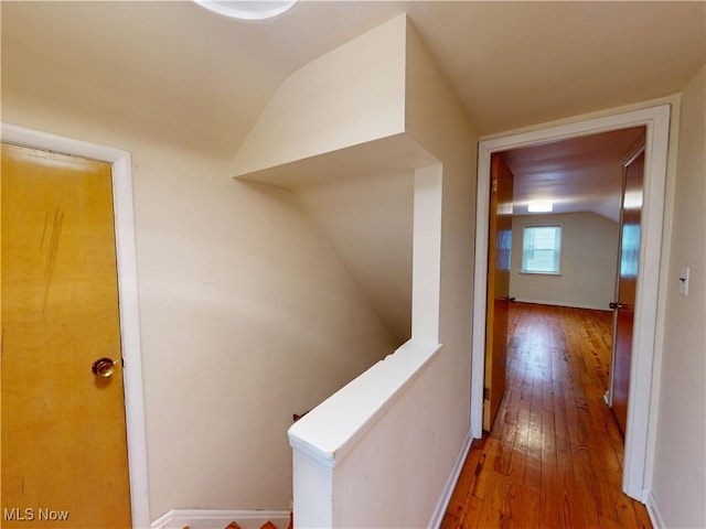 hallway with lofted ceiling, hardwood / wood-style floors, and an upstairs landing