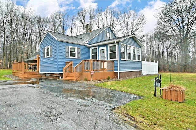 view of front of home with roof with shingles, a deck, and a front lawn