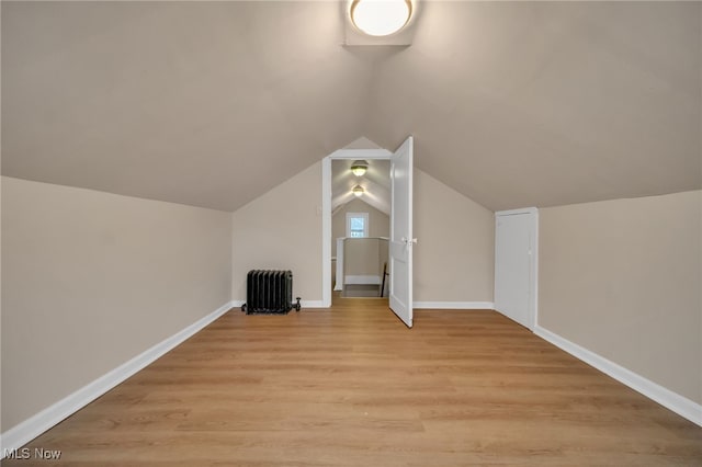 additional living space with baseboards, vaulted ceiling, light wood-type flooring, and radiator