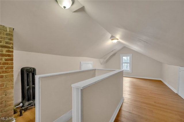 additional living space with vaulted ceiling, radiator heating unit, light wood-type flooring, and baseboards