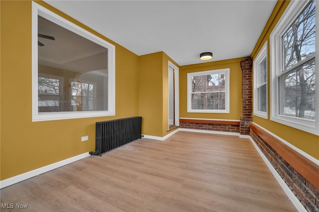 spare room featuring a wealth of natural light, baseboards, brick wall, and wood finished floors