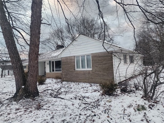 view of snow covered exterior featuring brick siding and a chimney