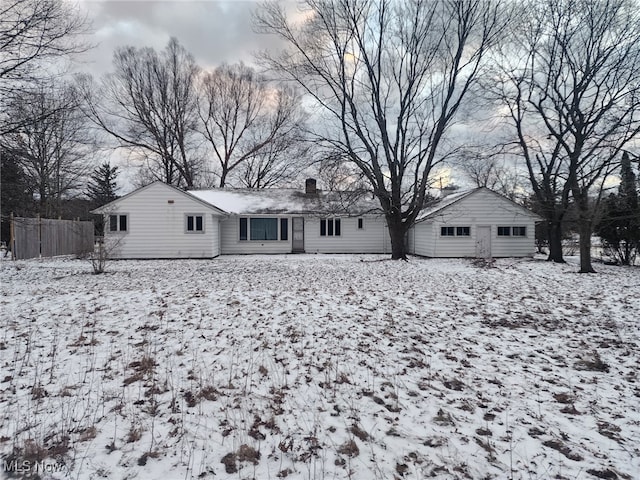 snow covered back of property featuring a chimney and fence