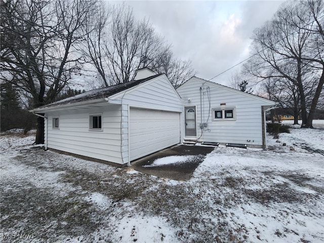 snow covered rear of property featuring a garage