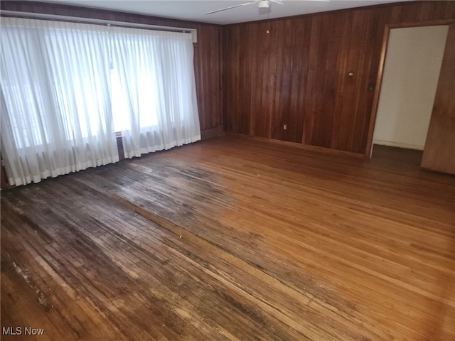 empty room featuring ceiling fan, wood walls, and wood finished floors