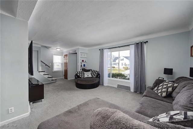 carpeted living room with visible vents, baseboards, stairway, and a textured ceiling