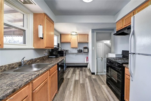 kitchen with under cabinet range hood, wood finished floors, a sink, black appliances, and dark countertops