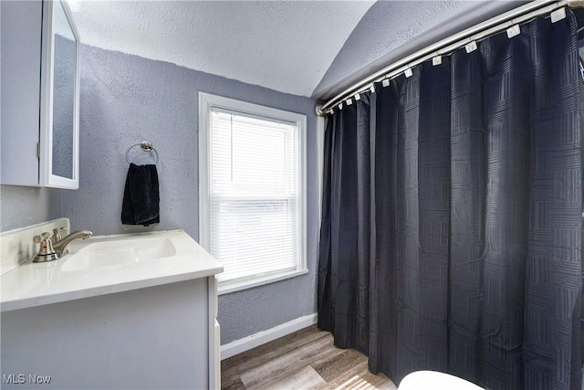 bathroom with lofted ceiling, a textured wall, wood finished floors, vanity, and baseboards