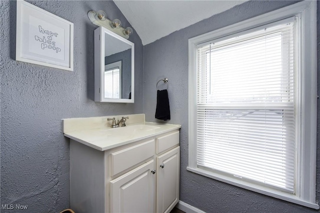 bathroom featuring vaulted ceiling, a textured wall, and vanity