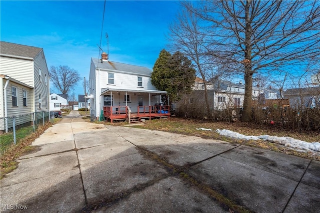 rear view of house featuring driveway, a chimney, fence, and a porch