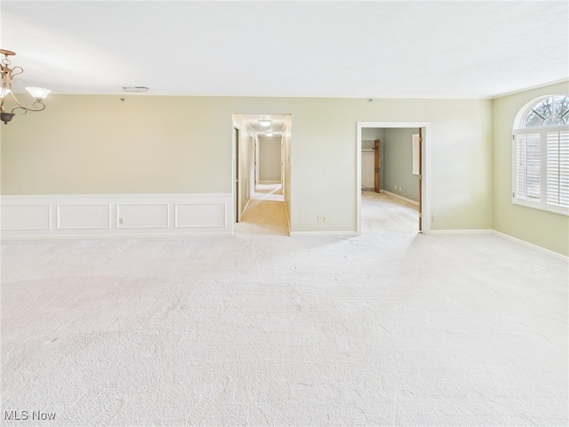 empty room featuring light carpet, baseboards, a chandelier, and a decorative wall