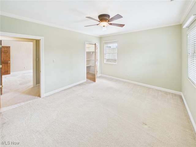 unfurnished bedroom featuring baseboards, a ceiling fan, light colored carpet, a walk in closet, and crown molding