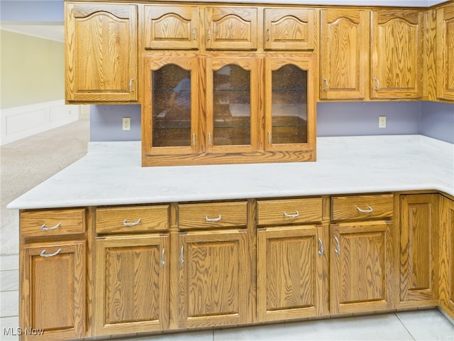 kitchen featuring glass insert cabinets, a wainscoted wall, light countertops, and brown cabinets