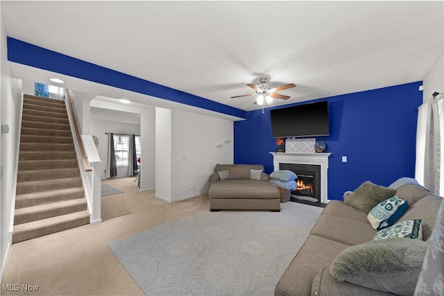 living area featuring ceiling fan, baseboards, stairway, carpet, and a glass covered fireplace