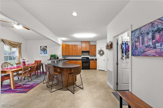 kitchen with brown cabinetry, dark countertops, a peninsula, a kitchen bar, and gas stove