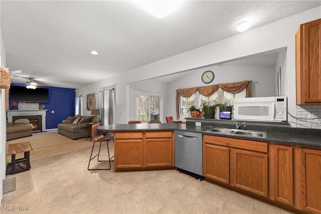 kitchen with a glass covered fireplace, white microwave, a peninsula, stainless steel dishwasher, and a sink