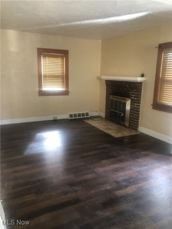 unfurnished living room with baseboards, visible vents, wood finished floors, a healthy amount of sunlight, and a brick fireplace