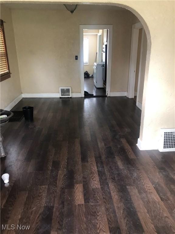 empty room featuring arched walkways, dark wood finished floors, visible vents, and baseboards