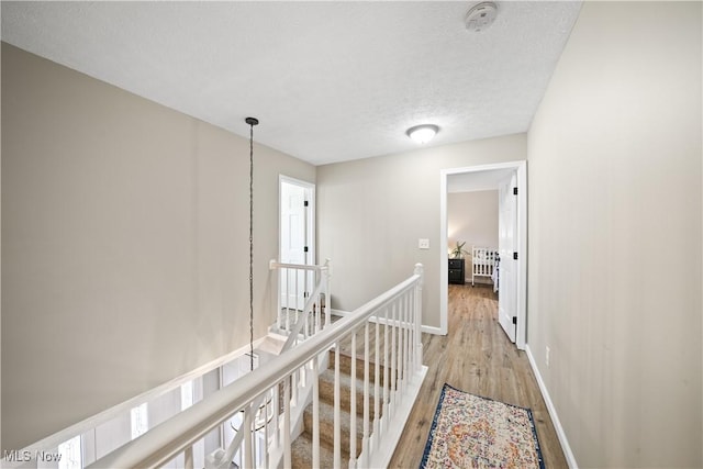 corridor featuring baseboards, a textured ceiling, an upstairs landing, and light wood-style floors