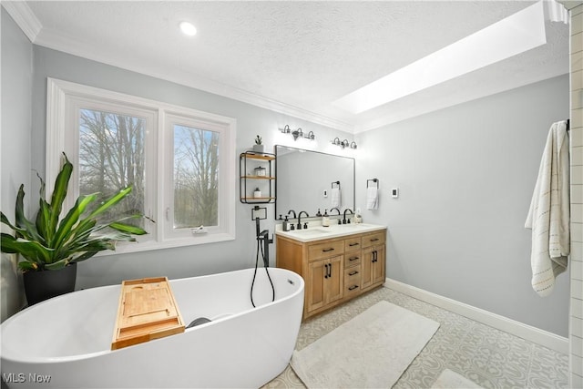 full bath featuring a textured ceiling, a freestanding tub, baseboards, double vanity, and crown molding