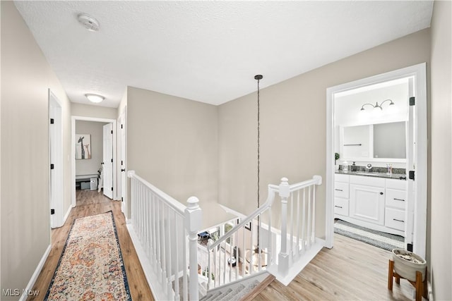 hallway featuring light wood-style flooring, baseboards, a textured ceiling, and an upstairs landing