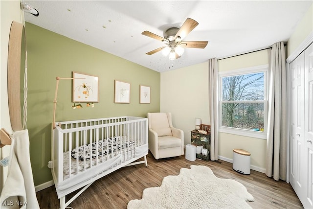 bedroom featuring ceiling fan, a crib, baseboards, and wood finished floors